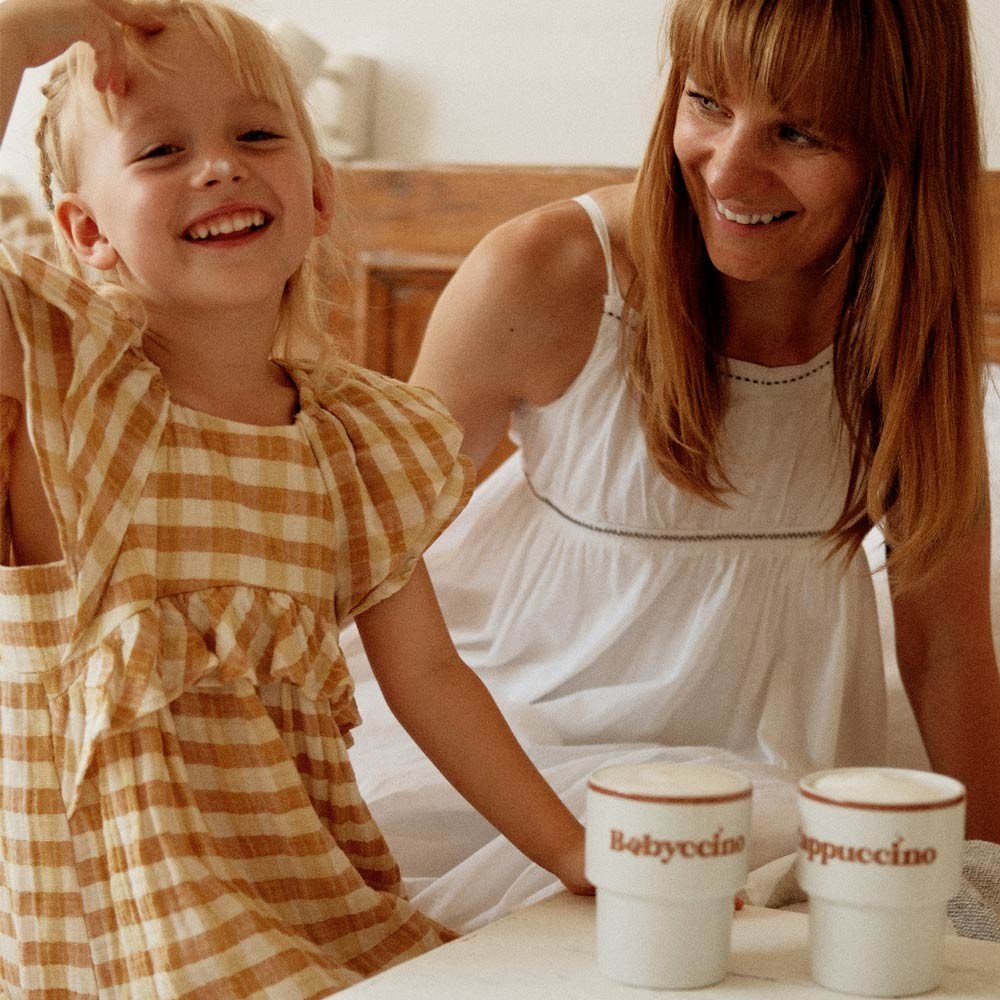 2. Woman and child enjoying drinks with Terra Mamma Babyccino ceramic mugs, child in yellow plaid dress, woman in white dress, indoors