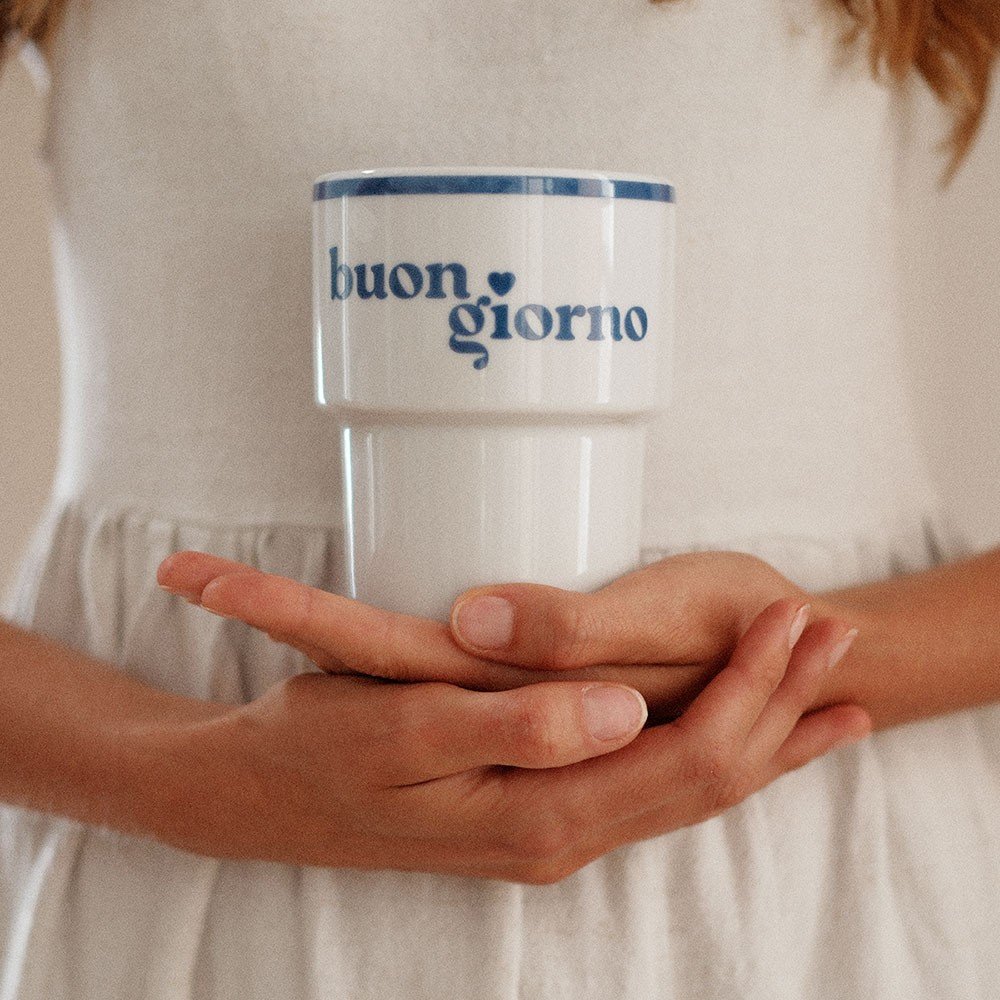 1. Woman in white dress holding Terra Mamma ceramic mug with 'buongiorno' text, indoors