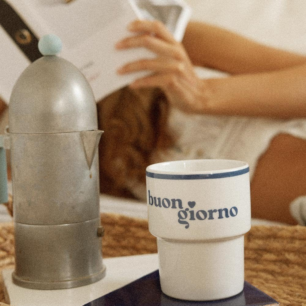 3. Terra Mamma ceramic mug with 'buongiorno' text on table next to coffee pot, woman reading in background