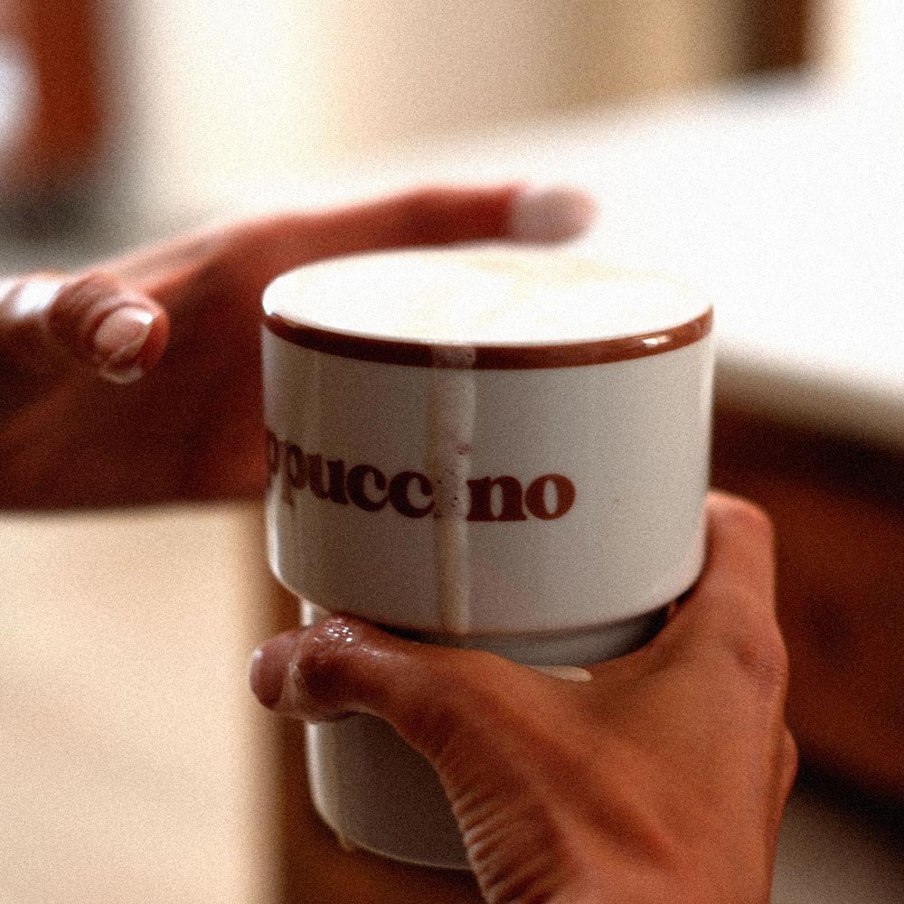 8. Hands holding Terra Mamma ceramic cappuccino mug with coffee spill