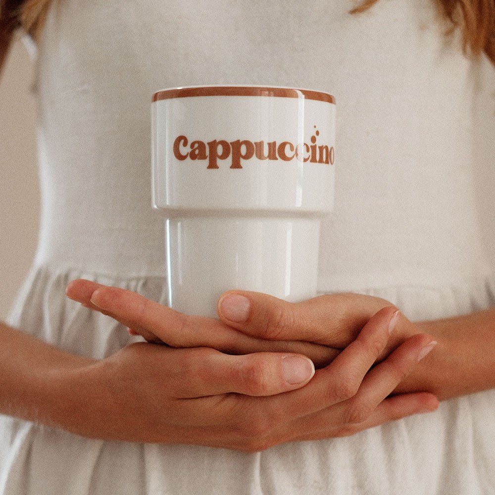 1. Woman in white dress holding Terra Mamma ceramic cappuccino mug with brown text