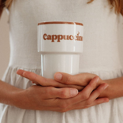1. Woman in white dress holding Terra Mamma ceramic cappuccino mug with brown text