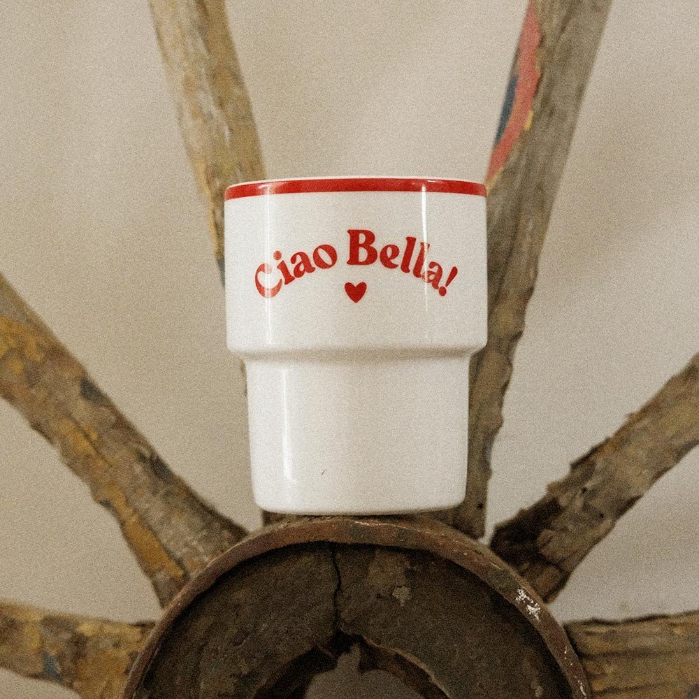 2. Terra Mamma 'Ciao Bella!' ceramic mug with red rim and text placed on rustic wagon wheel