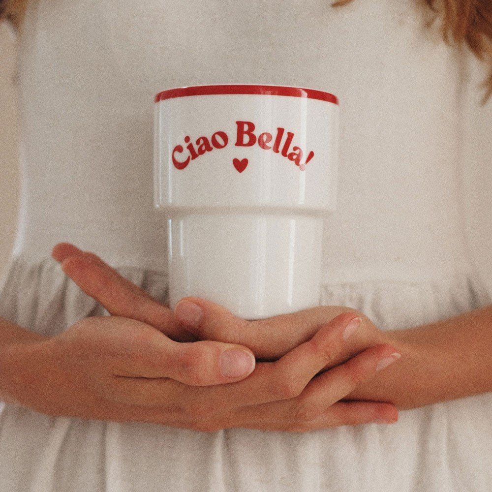 1. Woman in white dress holding Terra Mamma 'Ciao Bella!' ceramic mug with red rim and text