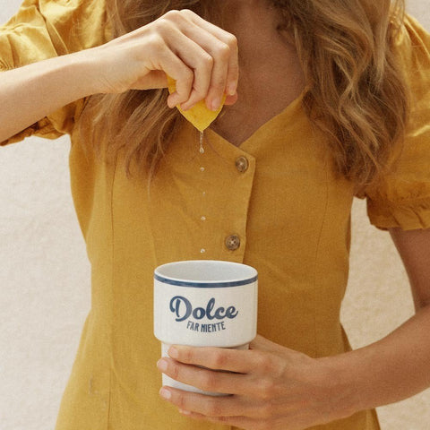 1. Woman in yellow dress squeezing lemon over Terra Mamma ceramic mug with 'Dolce far Niente' text