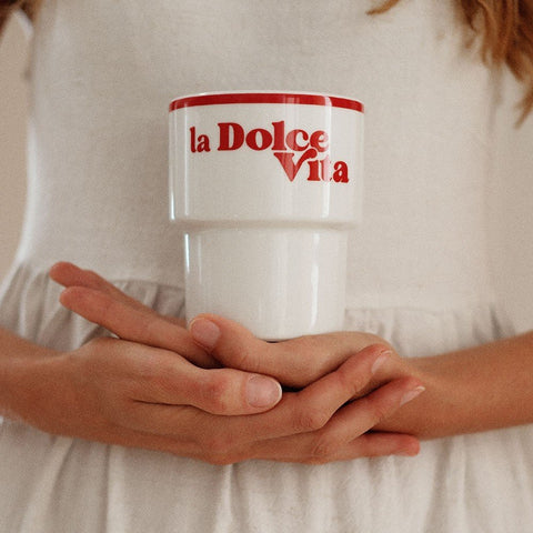 1. Woman holding Terra Mamma 'La Dolce Vita' ceramic mug with red text, wearing white dress, indoors
