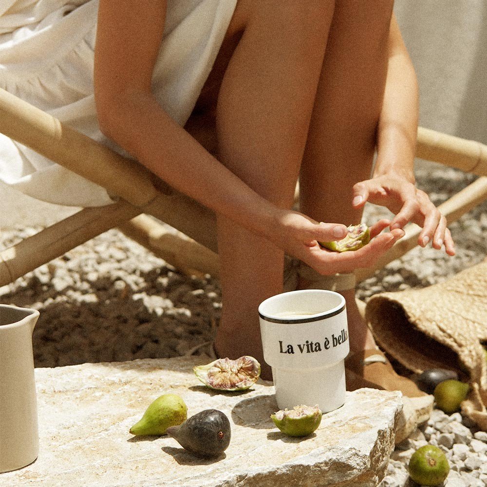 4. Woman seated outdoors with Terra Mamma ceramic mug and fresh figs, embodying Italian lifestyle