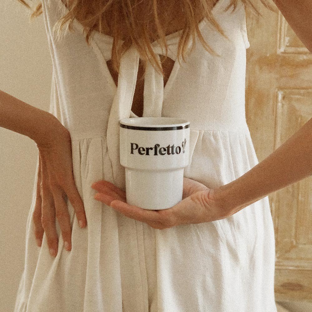 4. Woman holding Terra Mamma Perfetto ceramic mug with 'Perfetto!' text behind her back, wearing a white dress