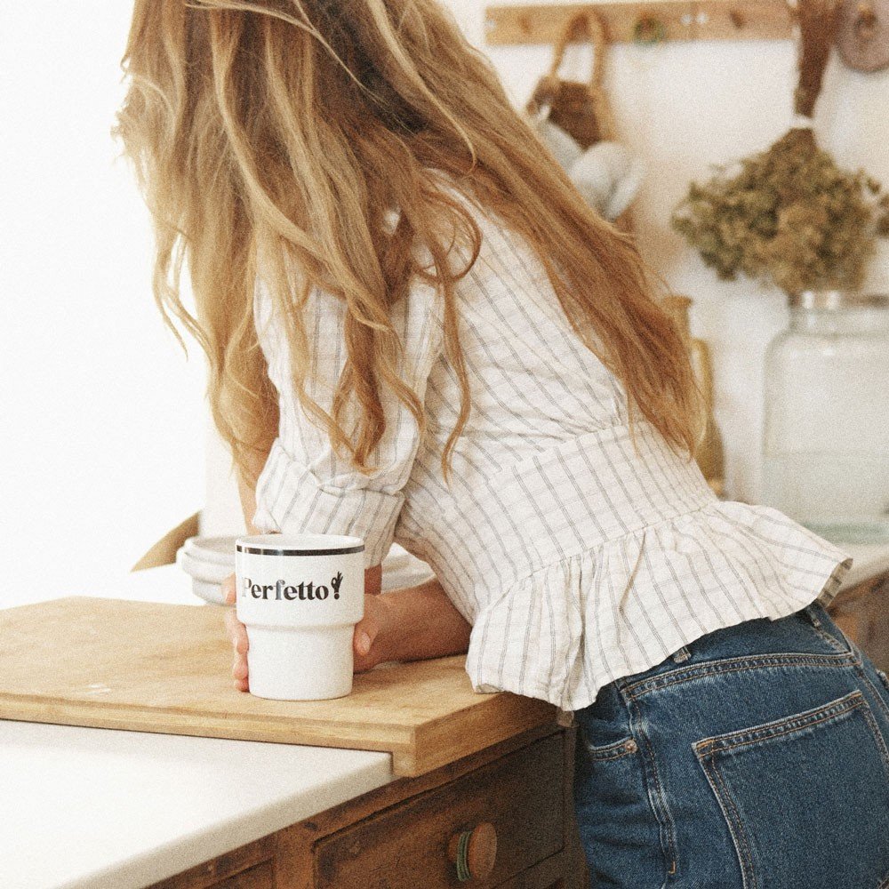 6. Woman leaning on a kitchen counter holding Terra Mamma Perfetto ceramic mug with 'Perfetto!' text, wearing a plaid blouse and jeans