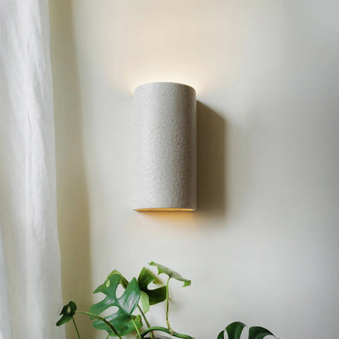 1. Beige spotted brown ceramic wall sconce on wall near window with plants, emitting soft light