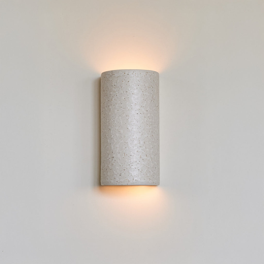 1. Beige spotted brown ceramic wall light sconce on white wall, emitting warm glow from top and bottom