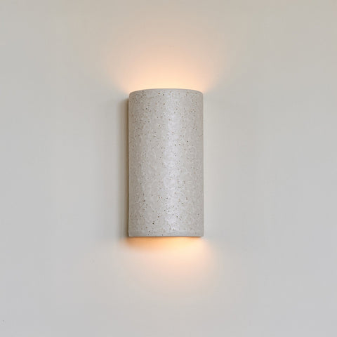 1. Beige spotted brown ceramic wall light sconce on white wall, emitting warm glow from top and bottom