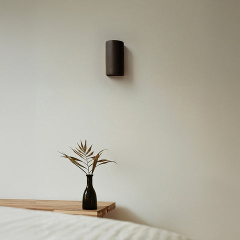 1. Brown ceramic wall light sconce by Ora in a minimalist bedroom setting with vase on table