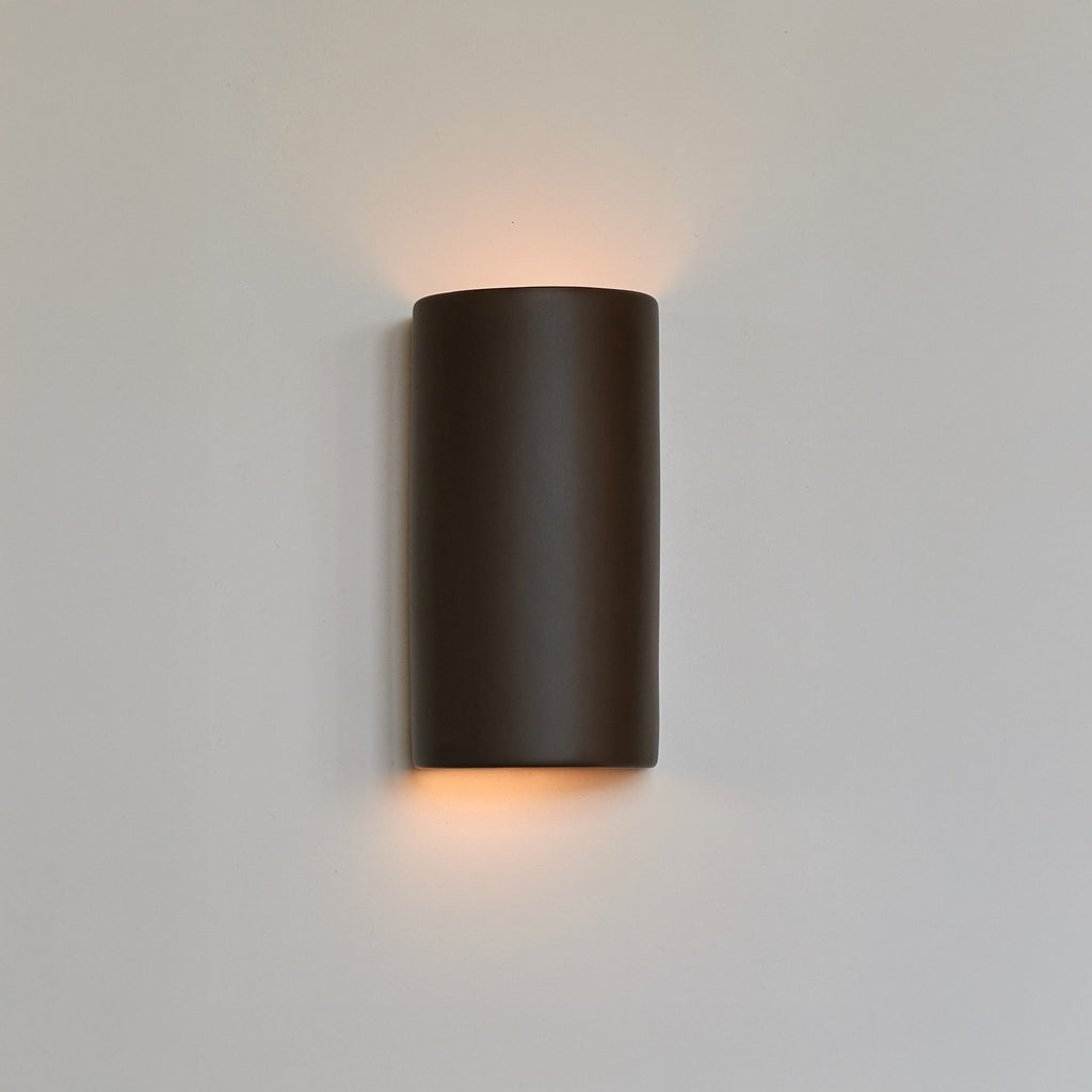 1. Brown ceramic wall light sconce by Ora illuminating a white wall with warm glow