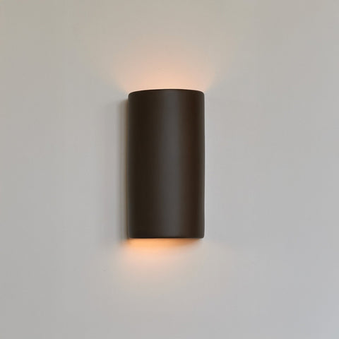 1. Brown ceramic wall light sconce by Ora illuminating a white wall with warm glow