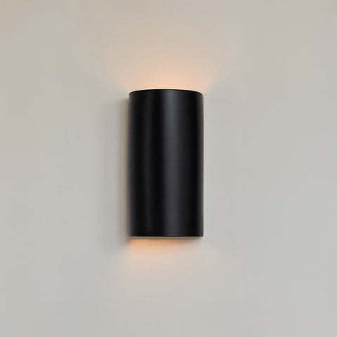 1. Black ceramic wall sconce by Ora on a light wall, emitting warm light from top and bottom