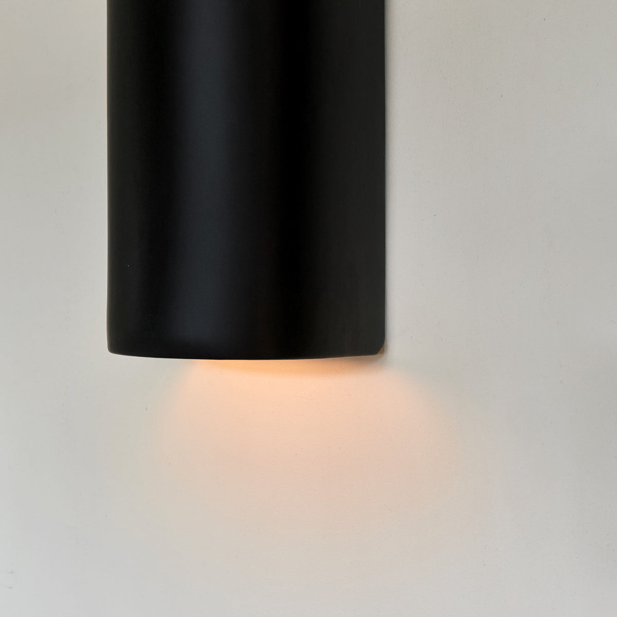 3. Close-up of black ceramic wall sconce by Ora with warm light glowing from bottom