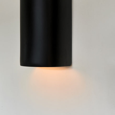 3. Close-up of black ceramic wall sconce by Ora with warm light glowing from bottom