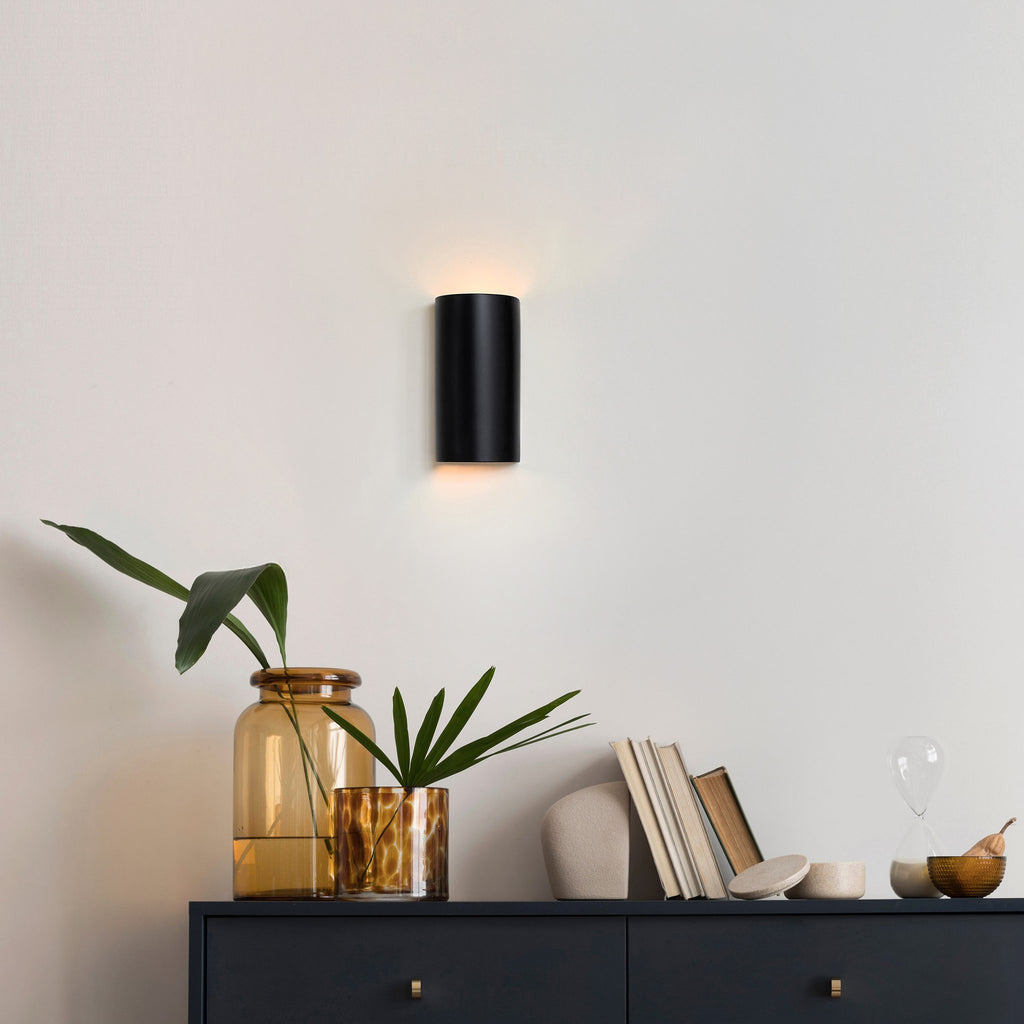 1. Black ceramic wall sconce by Ora illuminating a modern room with decor elements