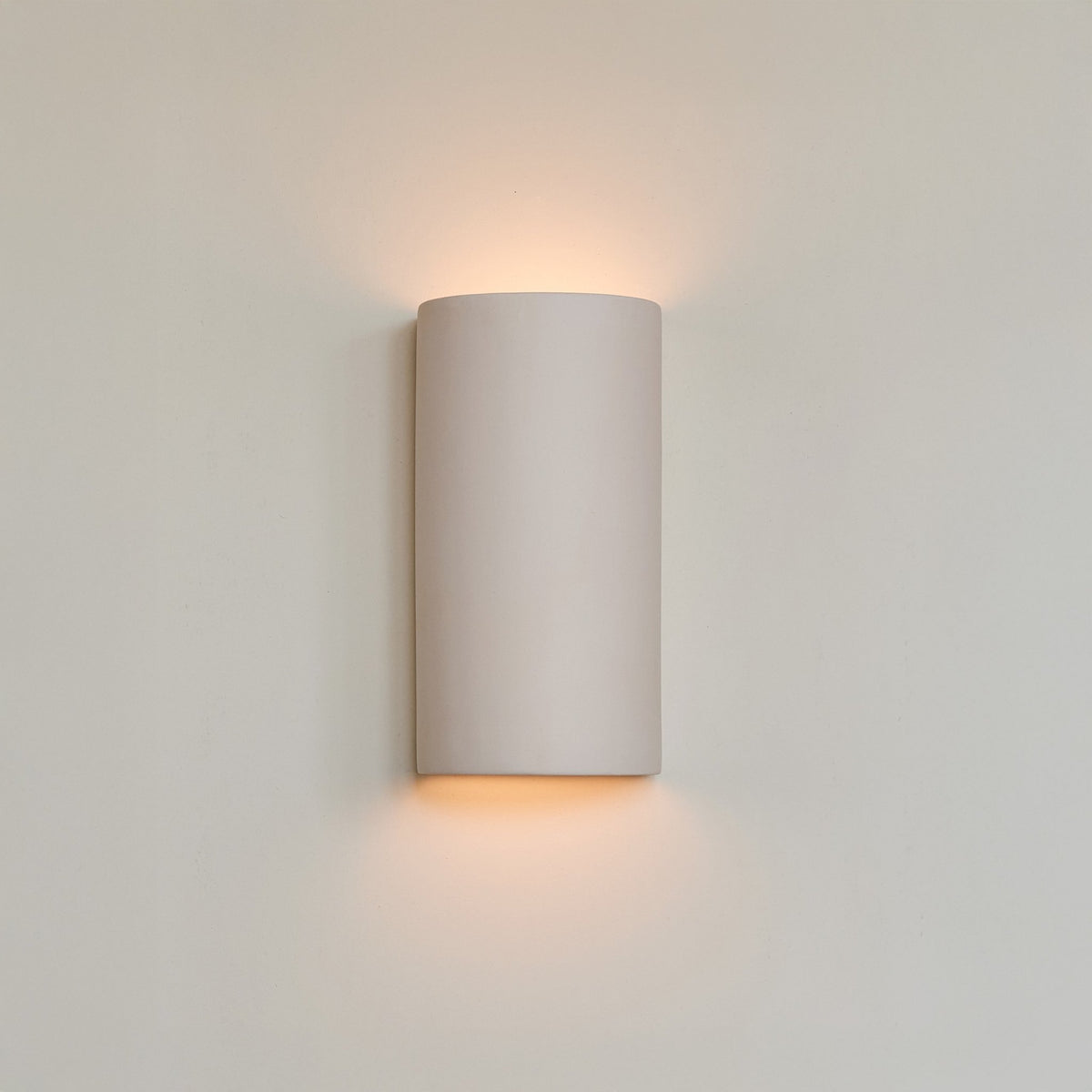1. Ceramic wall light in extra matte white with warm glow on neutral wall