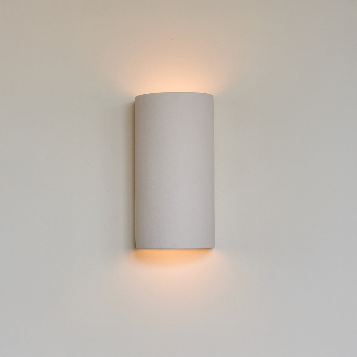 1. Extra matte white textured ceramic wall light by Ora, mounted on a wall, emitting a warm glow from top and bottom.
