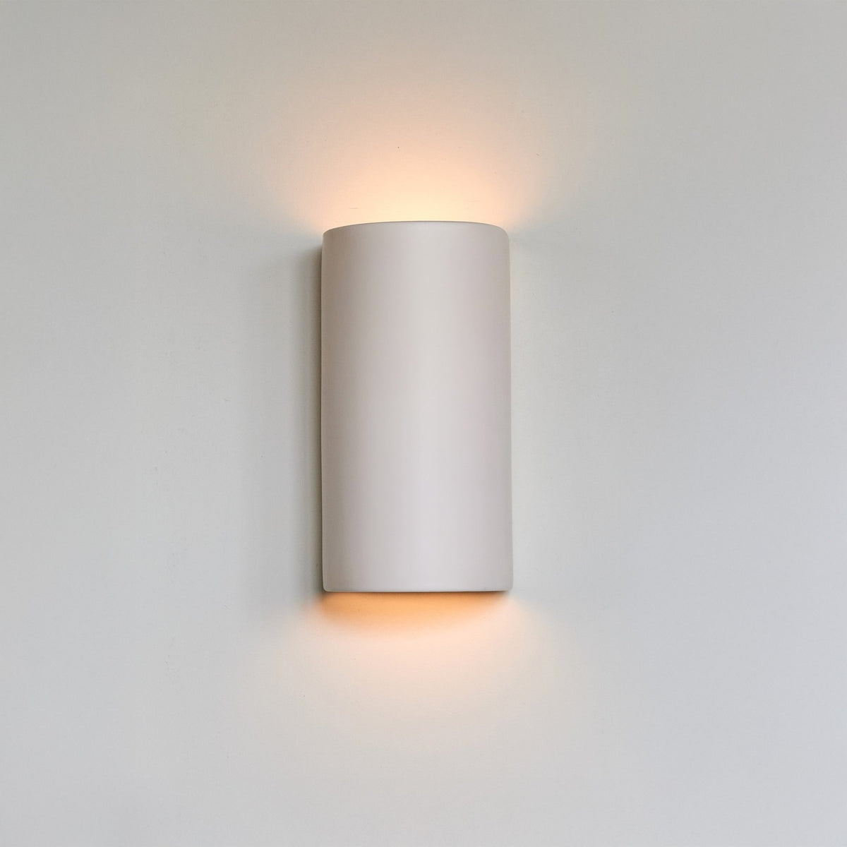 1. Off-white ceramic wall sconce by Ora with warm glow against a plain wall