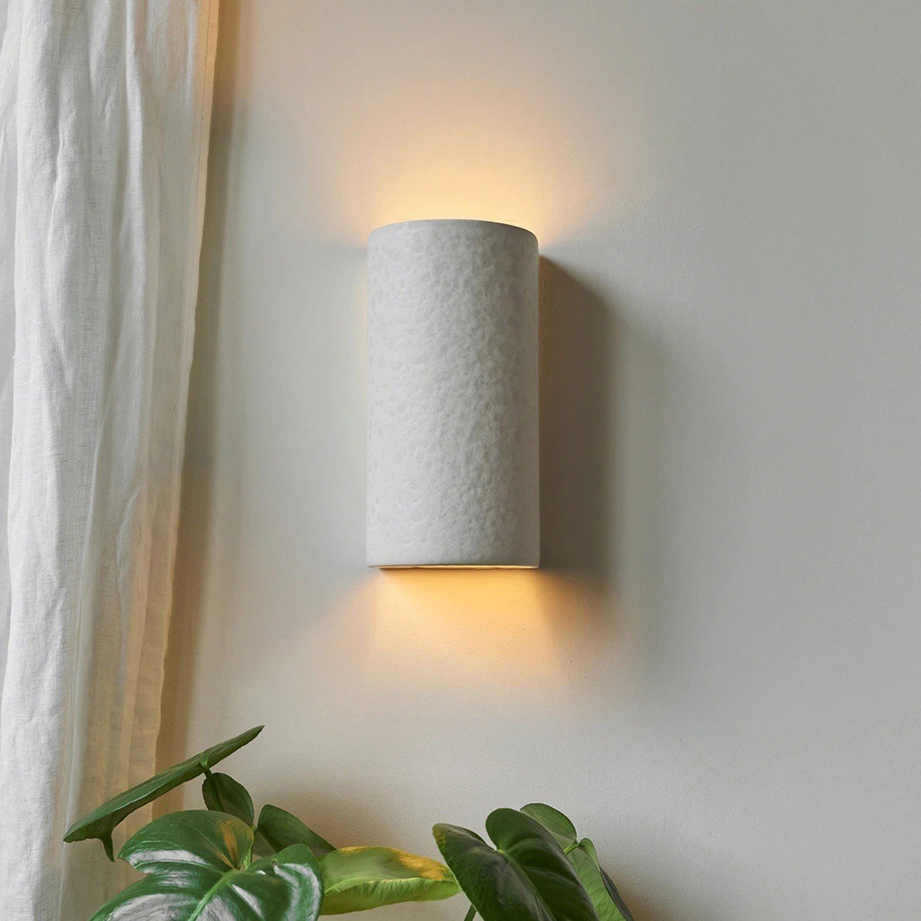 1. Ceramic wall light in raw white with warm glow next to plants