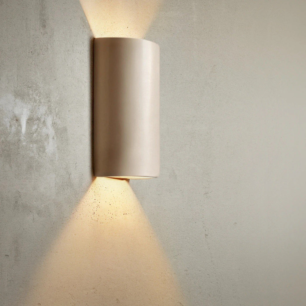8. Taupe ceramic wall light sconce on textured wall, casting warm light upwards and downwards