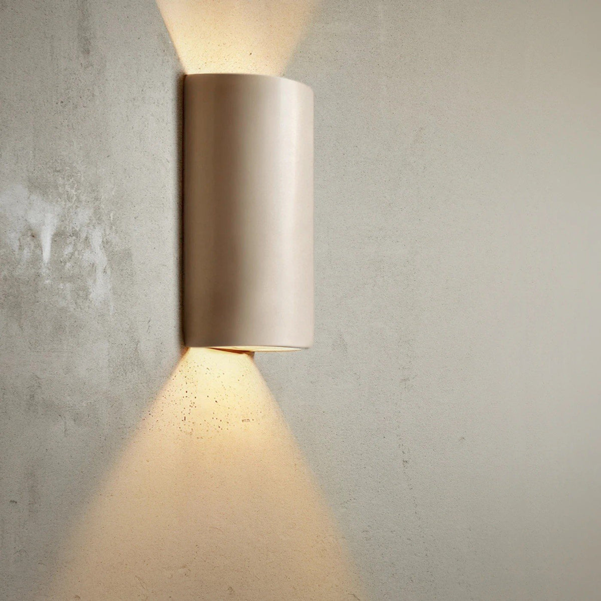 8. Taupe ceramic wall light sconce on textured wall, casting warm light upwards and downwards