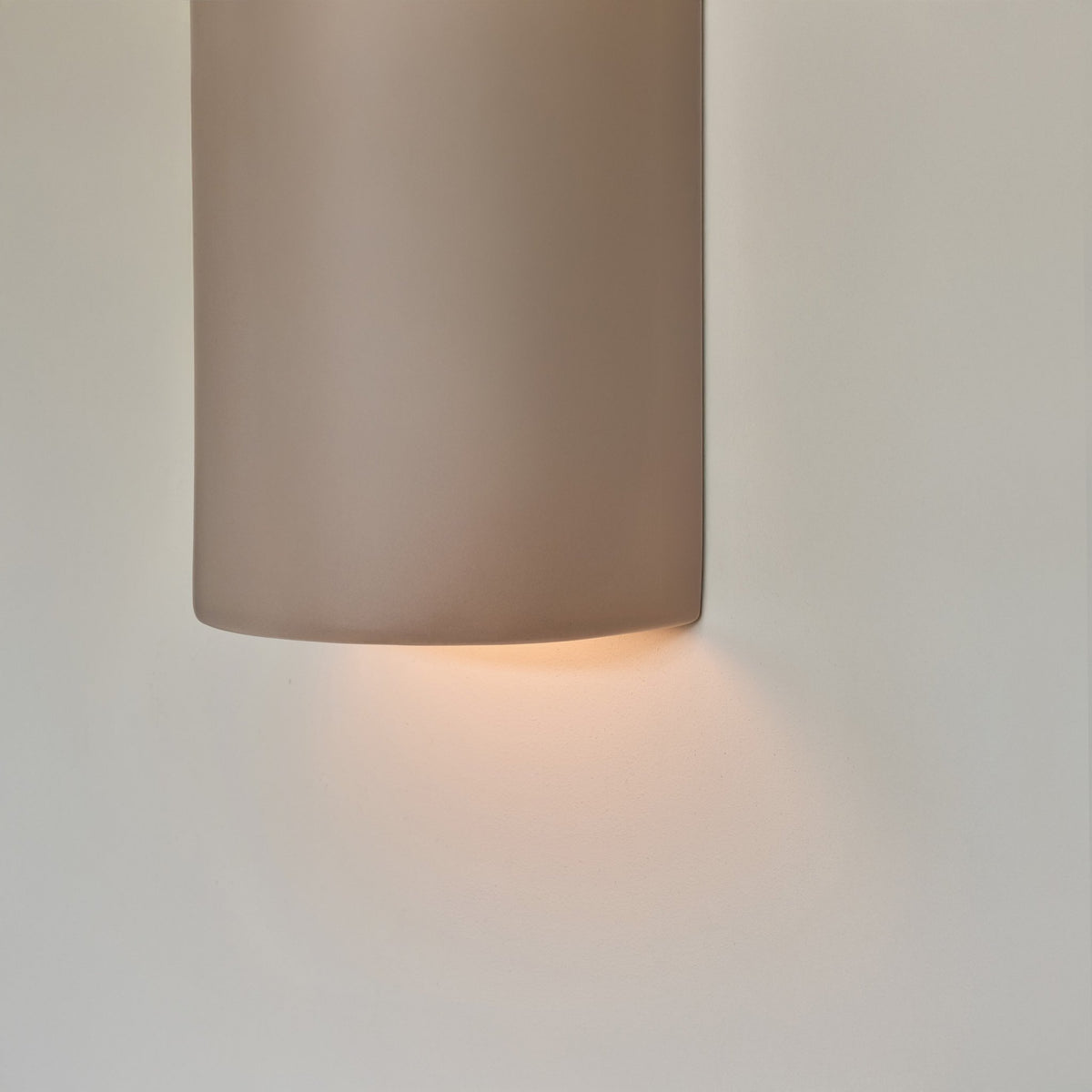 3. Detail of taupe ceramic wall light sconce with soft light glowing from bottom, highlighting smooth texture