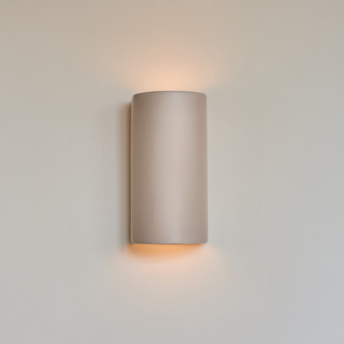 1. Taupe ceramic wall light sconce mounted on a white wall, emitting a warm glow from top and bottom, showcasing minimalist design