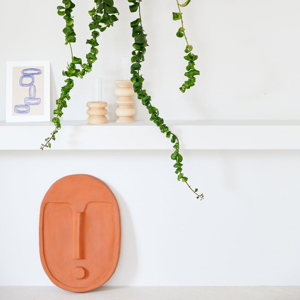 2. Terracotta orange ceramic wall mask by 5mm Paper displayed on a shelf with greenery and decor