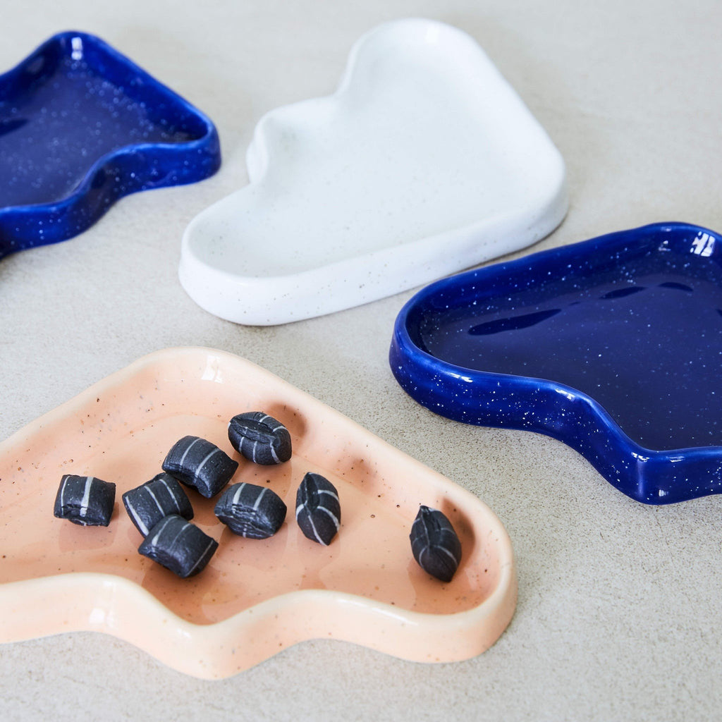 1. Lifestyle image of 5mm Paper Ceramic Wave Trays in blue, white, and peach, displayed on a surface with small items