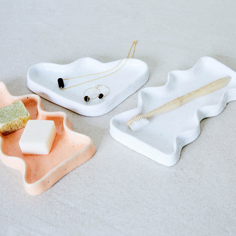 1. Lifestyle image of 5mm Paper Ceramic Wave Tray in white and peach, holding jewelry and toiletries on a bathroom counter