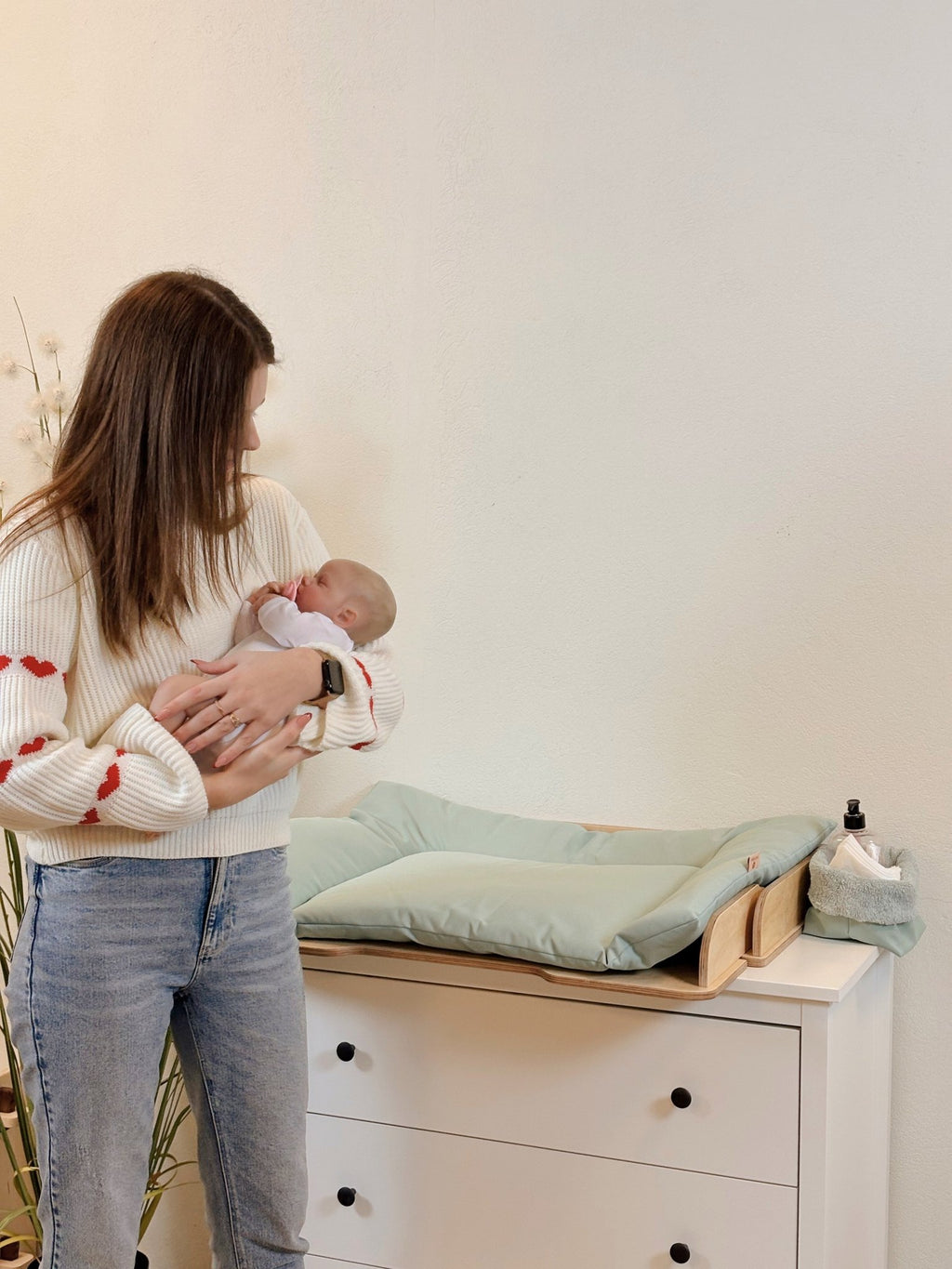 2. Woman holding baby next to green changing table mat on a dresser
