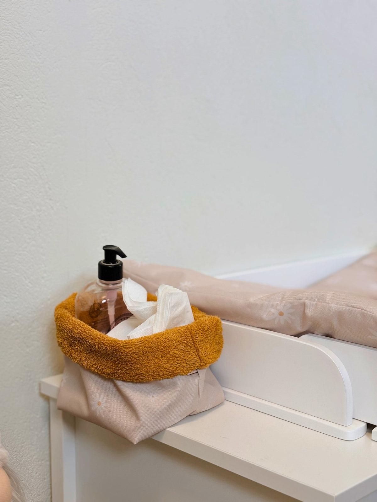 5. Beige changing table storage basket with mustard lining holding a pump bottle and tissues on a white changing table
