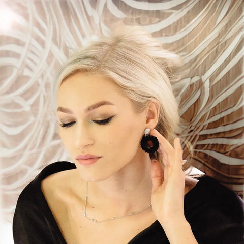 1. Woman wearing MyaMoon Cherie Boho L earrings in rose gold and silver with black spinel pearl rings, set against a patterned background