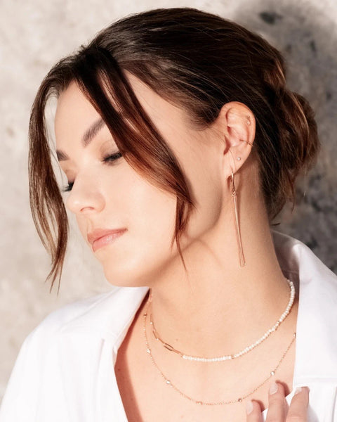 1. Woman wearing MyaMoon Cherie L-Tassel Earrings in rose gold, styled with layered necklaces, showcasing elegant design in lifestyle setting