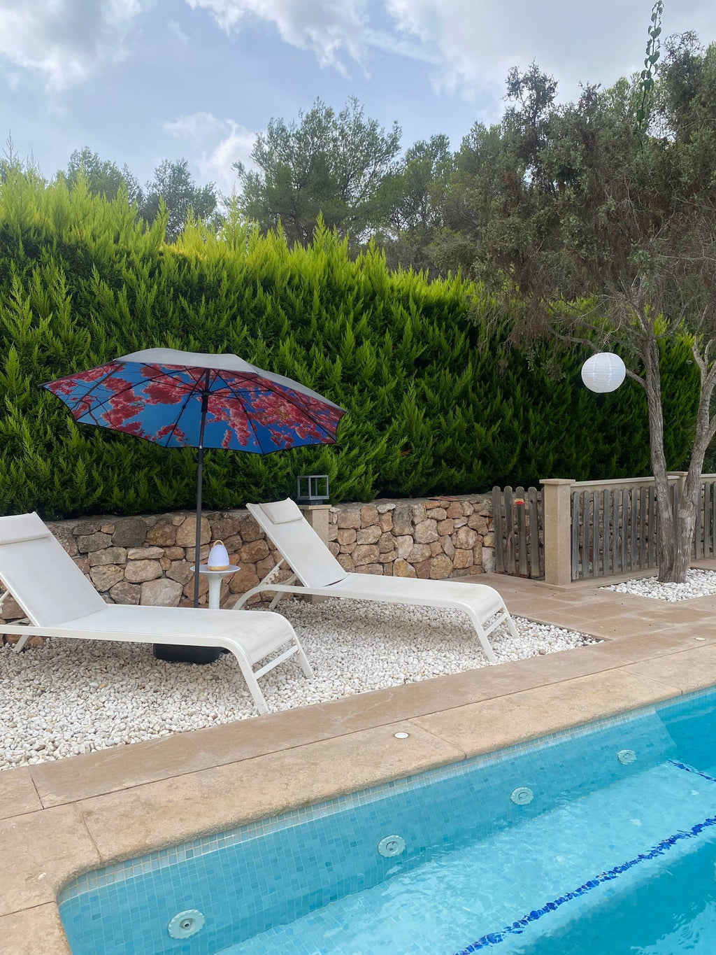 2. Cherry beach and terrace parasol with red floral design by a poolside with two white sun loungers