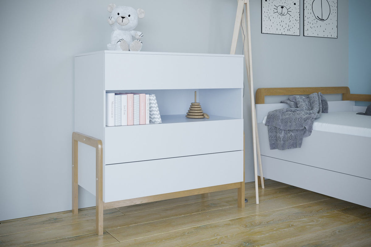 1. White chest of drawers with oak legs in a child's room, featuring books and a teddy bear on top