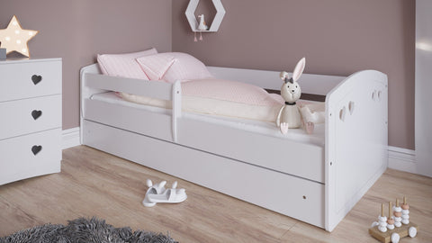 4. White children's bed with heart cutouts and pink bedding in a pastel room with plush toys