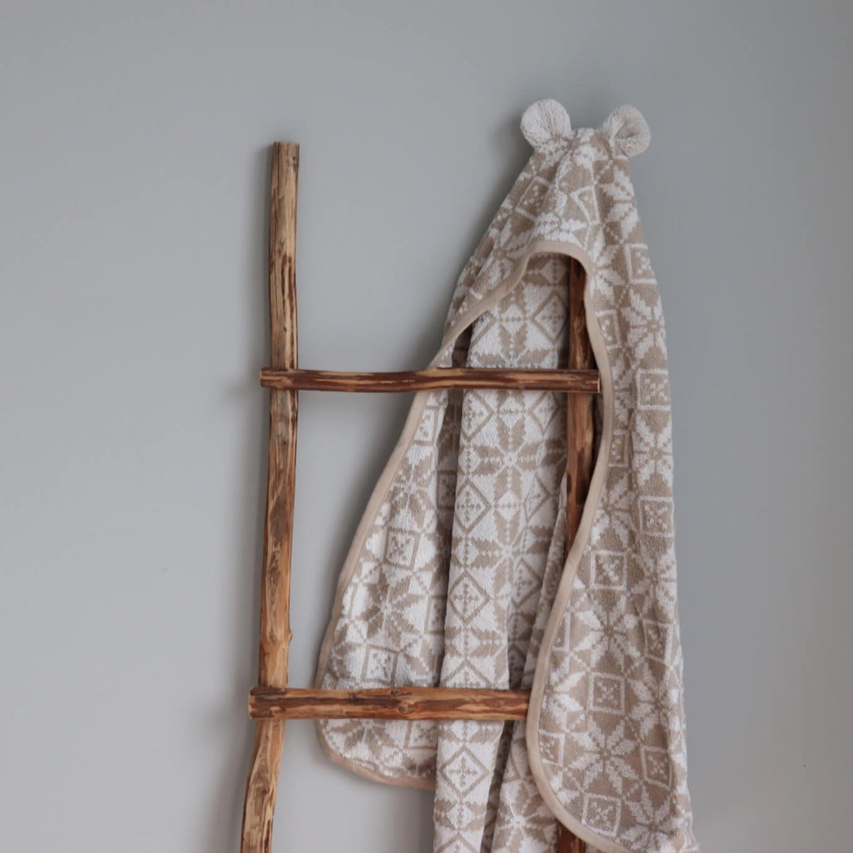 1. Beige children's hooded towel with teddy bear ears and Hiiumaa mitten pattern hanging on wooden ladder