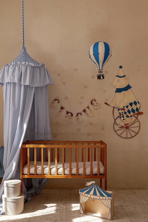 3. Nursery wall featuring a teddy bear on a bike, blue hot air balloon, and circus banner above a wooden crib with a blue canopy.