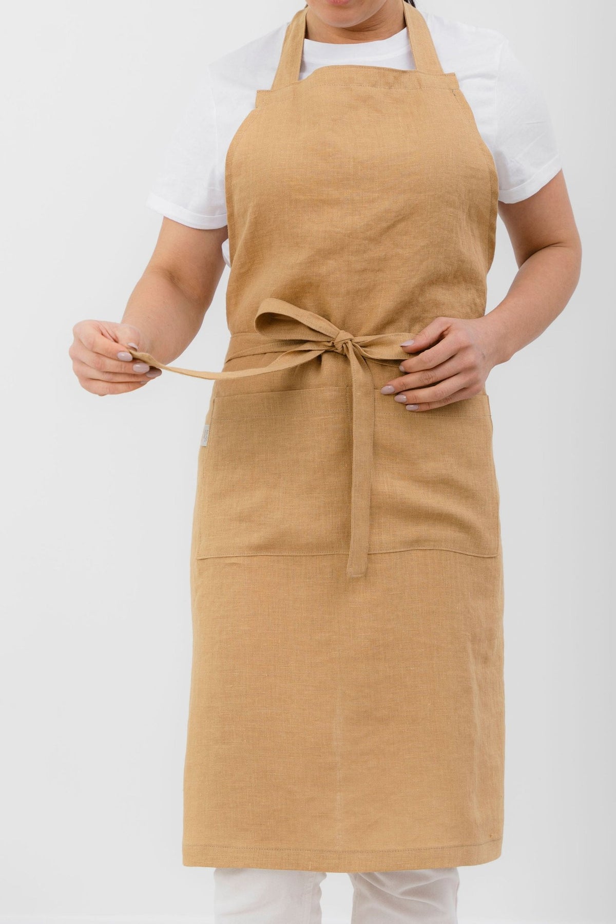 8. Woman in mustard yellow linen apron with front pocket, tied at waist, against white background