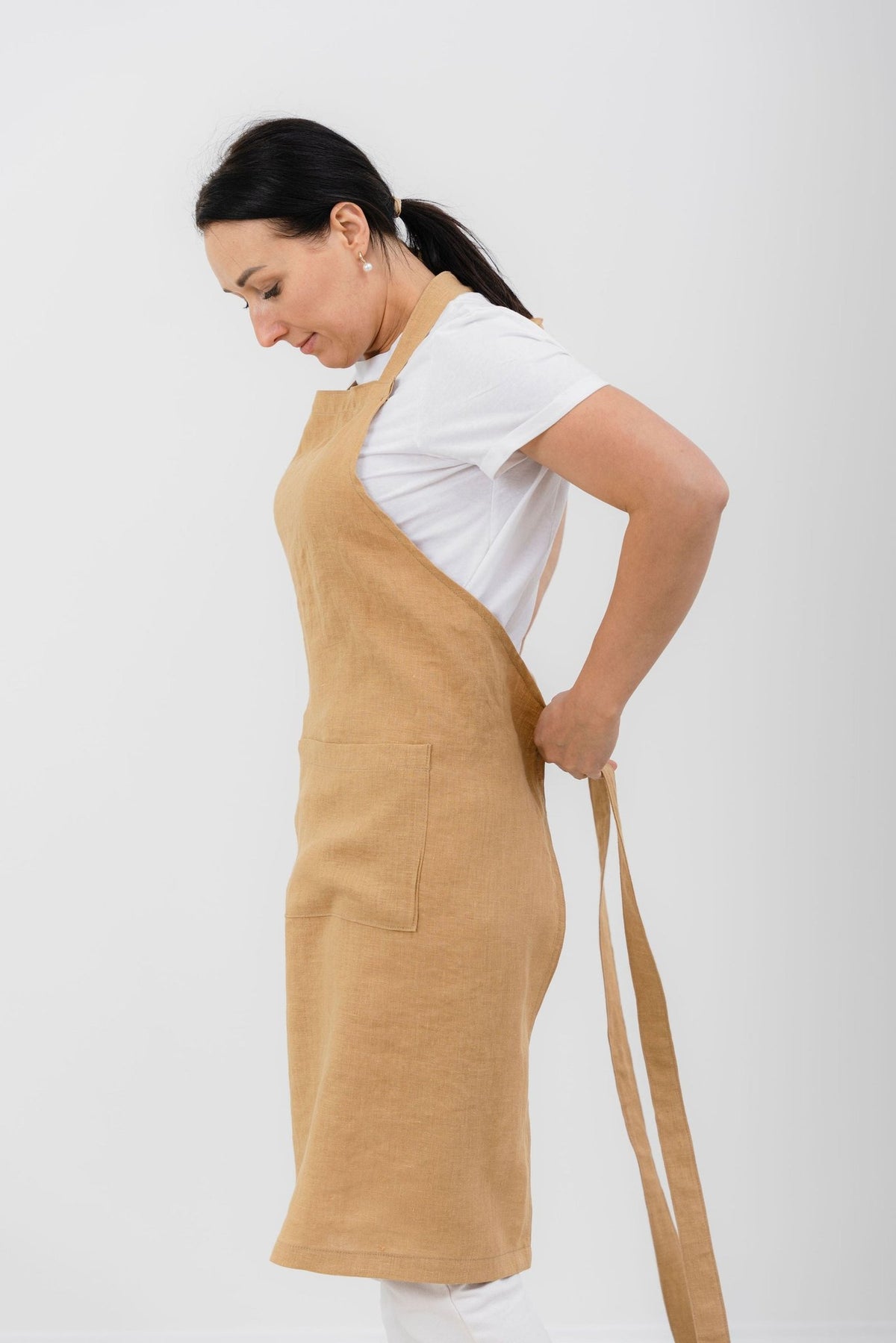 9. Woman tying mustard yellow linen apron at back, showing side view and front pocket