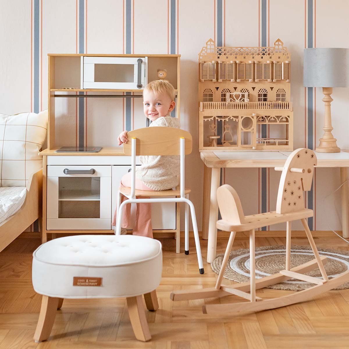 3. Child in a playroom with classic stripes wallpaper in linen beige, soft blue, and muted red, surrounded by wooden toys and furniture
