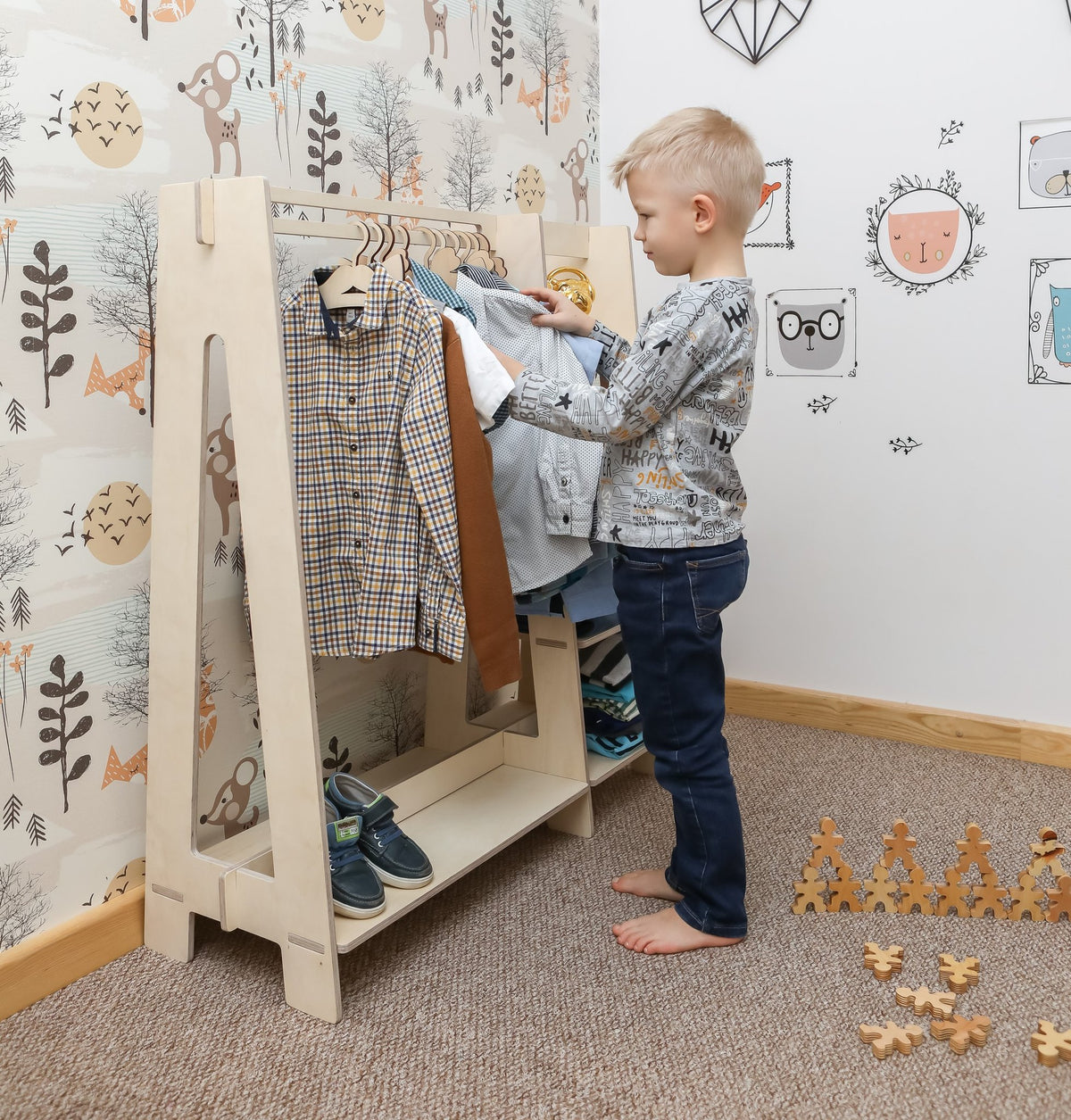 3. Boy interacting with natural wood clothing rack in a nursery setting with playful wallpaper