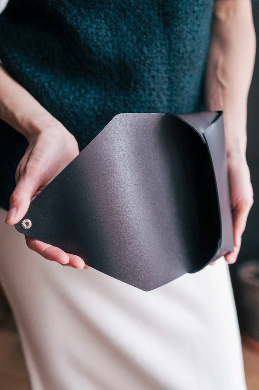 4. Close-up of open black leather clutch bag showing interior, held by woman in teal sweater