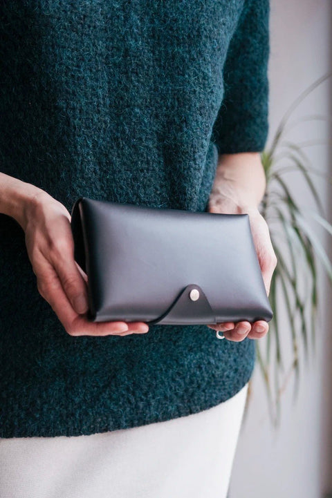 5. Close-up of black leather clutch bag with snap closure, held by woman in teal sweater