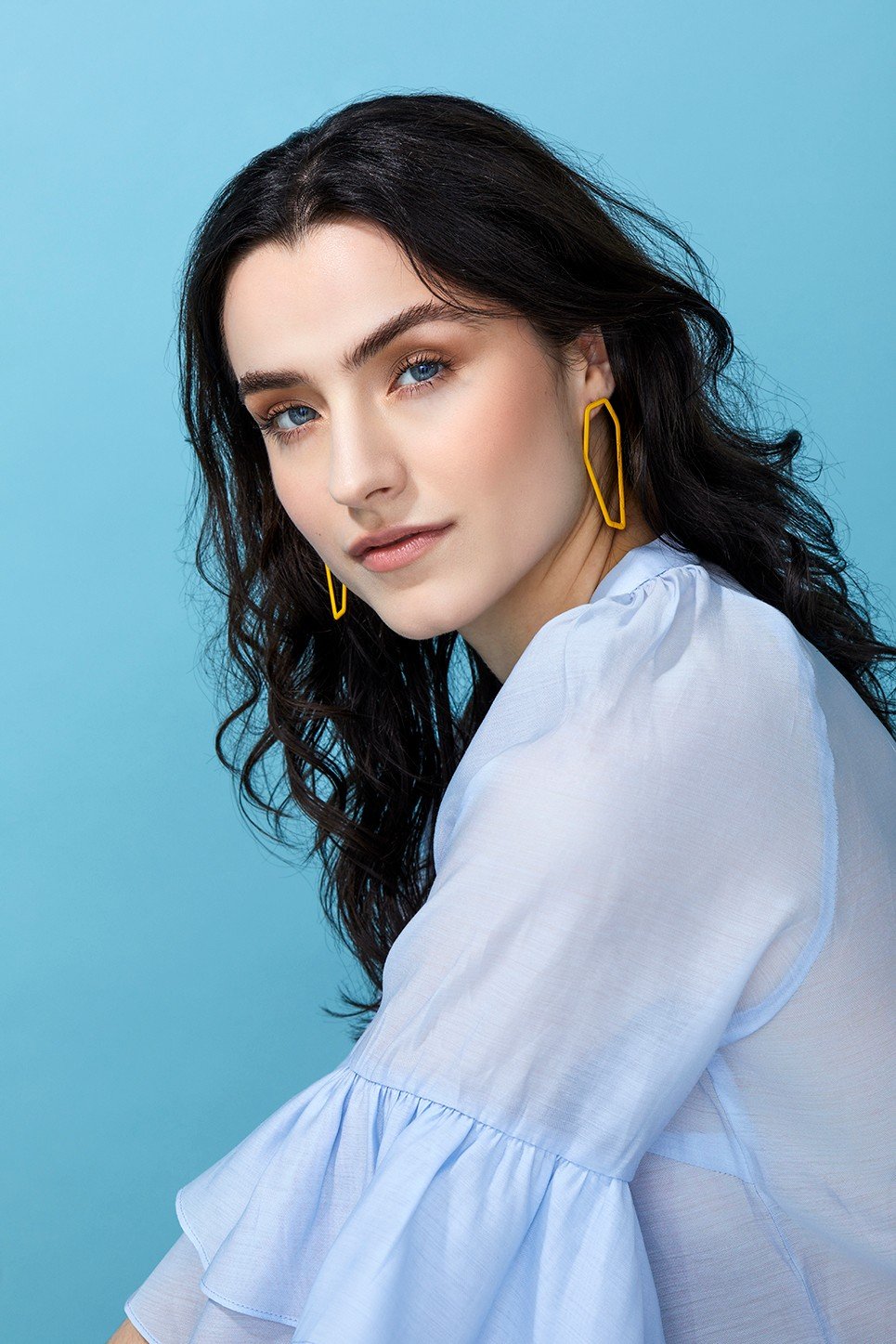 1. Woman wearing Lisa Kroeber Jewellery Color Frames Earrings in yellow, styled with a light blue blouse against a blue background